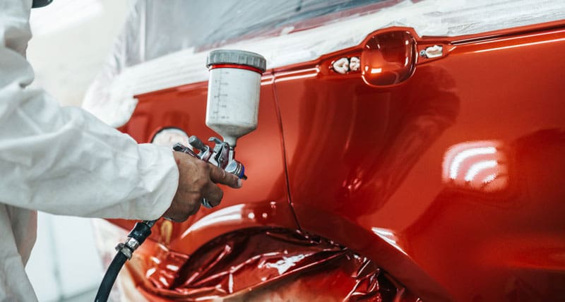 Man painting car red using spray compressor
