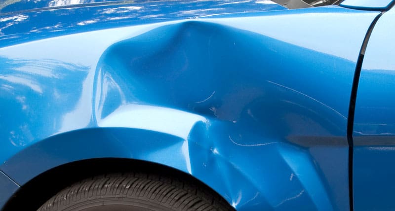 A blue car with a large dent in the front fender