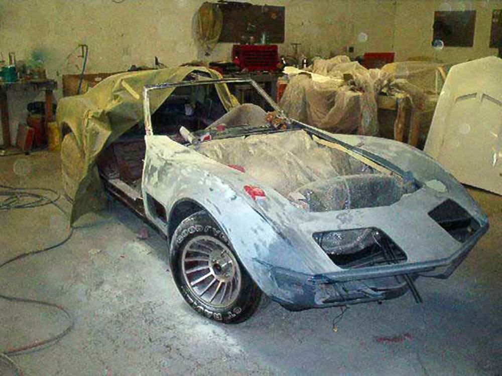 Image of a classic red Corvette convertible in a workshop, stripped and prepped for painting.