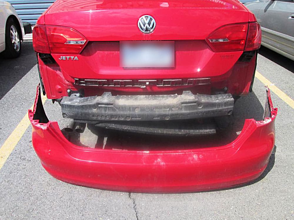 Image of a red Volkswagen Jetta with its rear bumper detached, showing underlying damage.