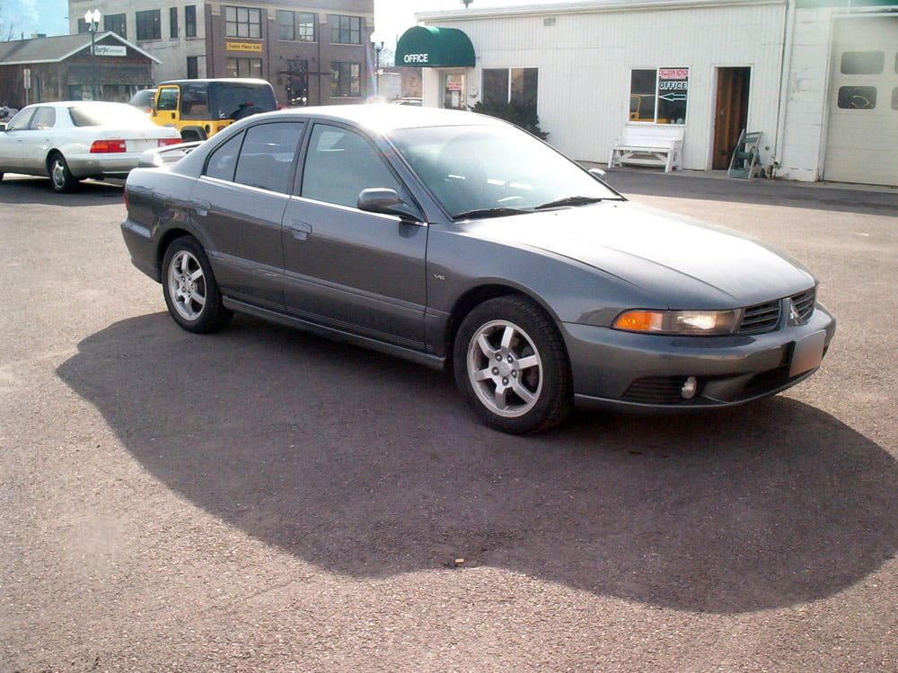 Same dark gray Mazda sedan after side impact repair, parked outside the shop. The same white car after dent and body repair, side view