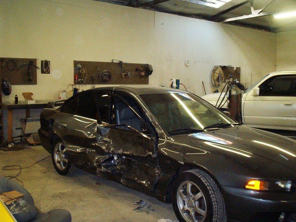 Dark gray Mazda sedan with severe side impact damage to the driver's doors