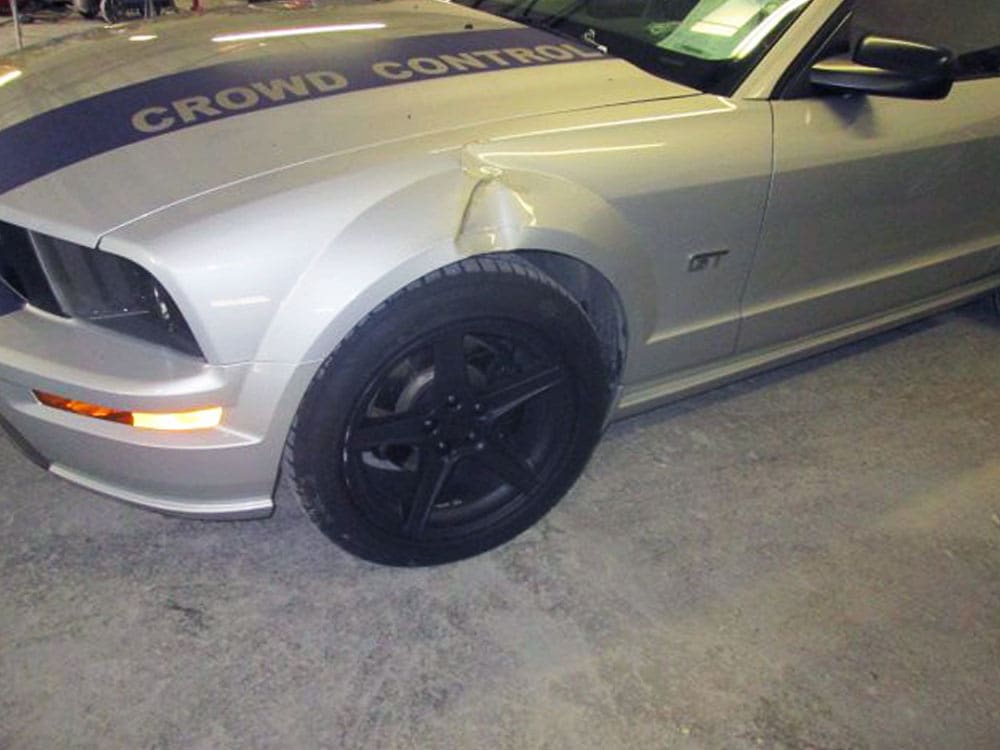 Silver Ford Mustang with a noticeable dent and crease on the front passenger fender.