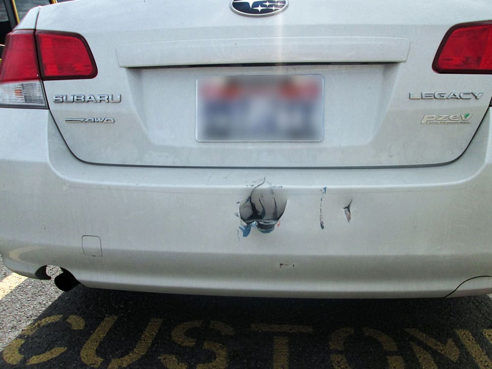 Image of a white Subaru Legacy with significant rear bumper impact damage and scrapes.
