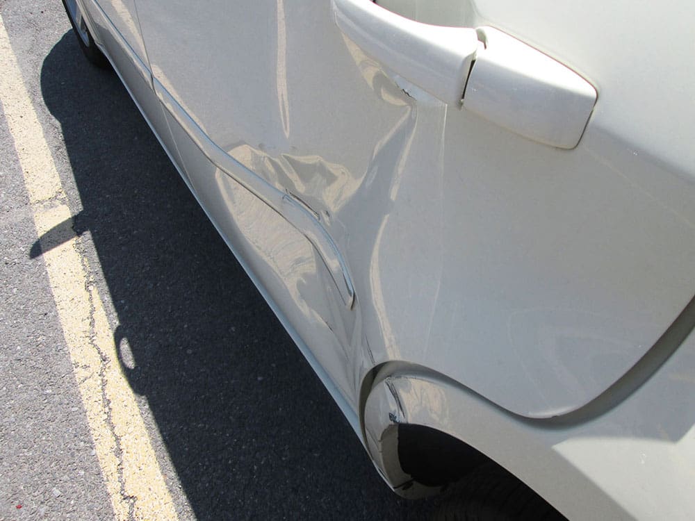 White car with significant dent damage on the rear passenger door and quarter panel.